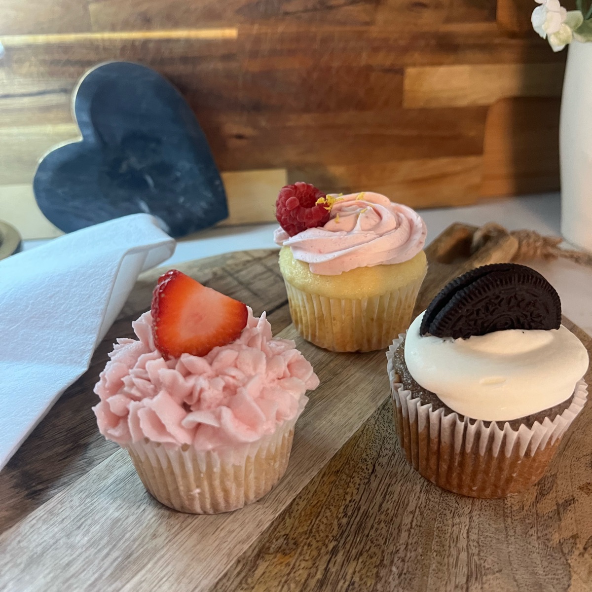 Three cupcakes: strawberry with pink ruffled buttercream, raspberry swirl, and chocolate with a cookie