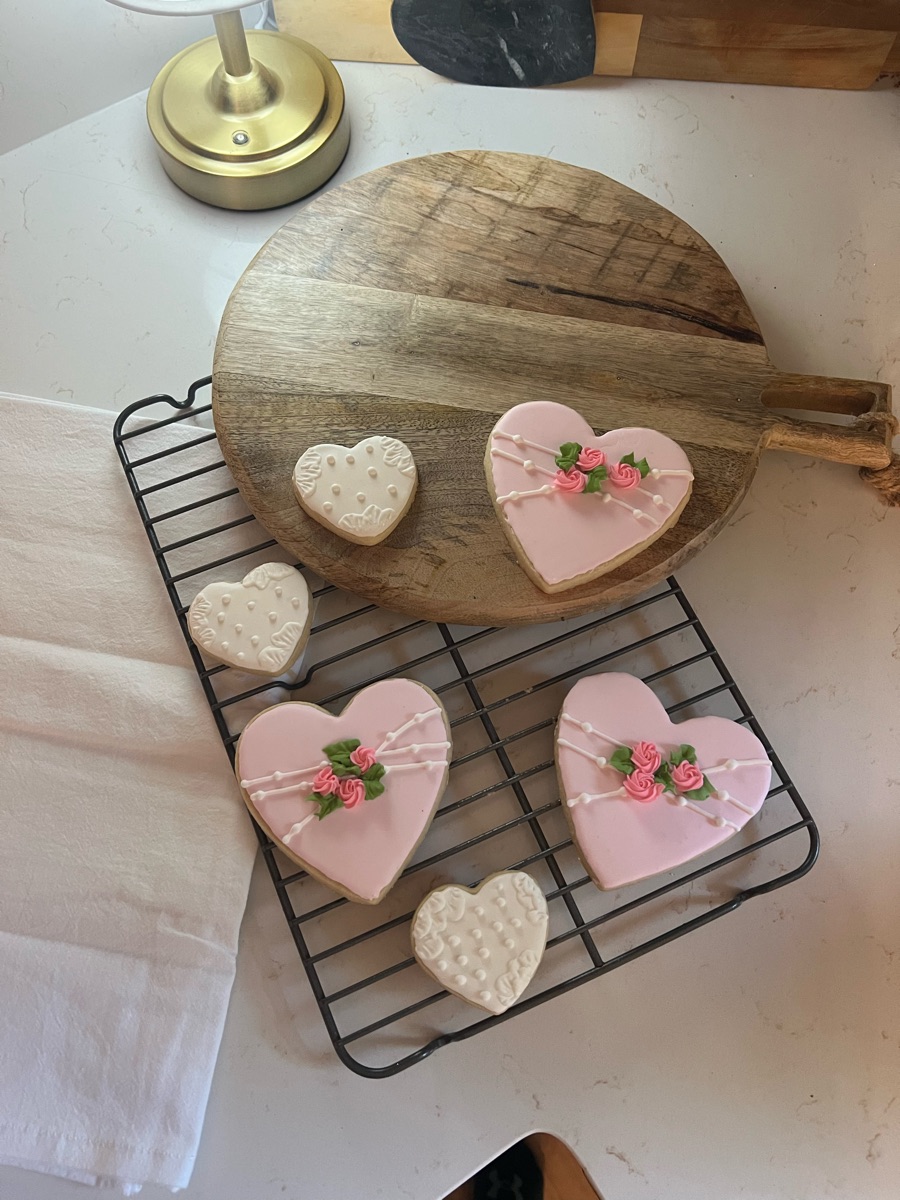 Pink heart cookies with piped roses and white lace heart cookies on a cooling rack