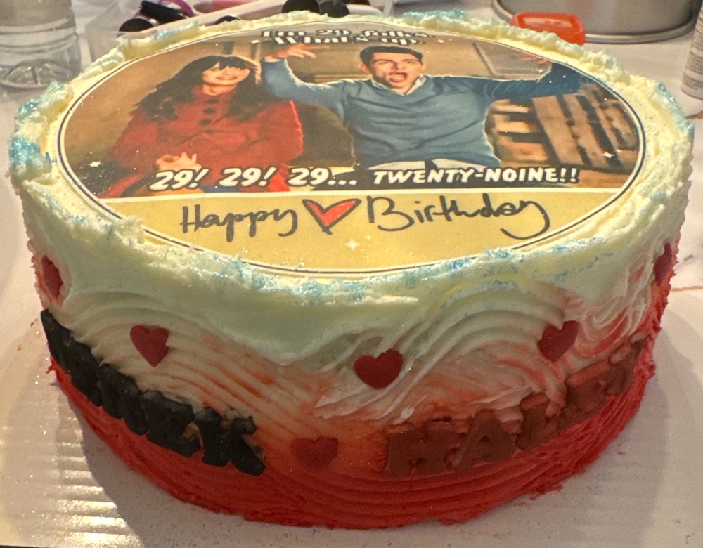 Red and white birthday cake with an edible TV show image reading 29! 29! 29... Twenty-Noine!! and Happy Birthday