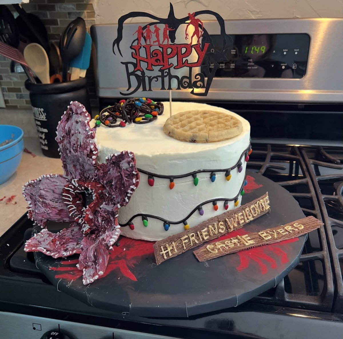 Stranger Things themed birthday cake with string lights, waffle topper, monster flower and wooden welcome signs